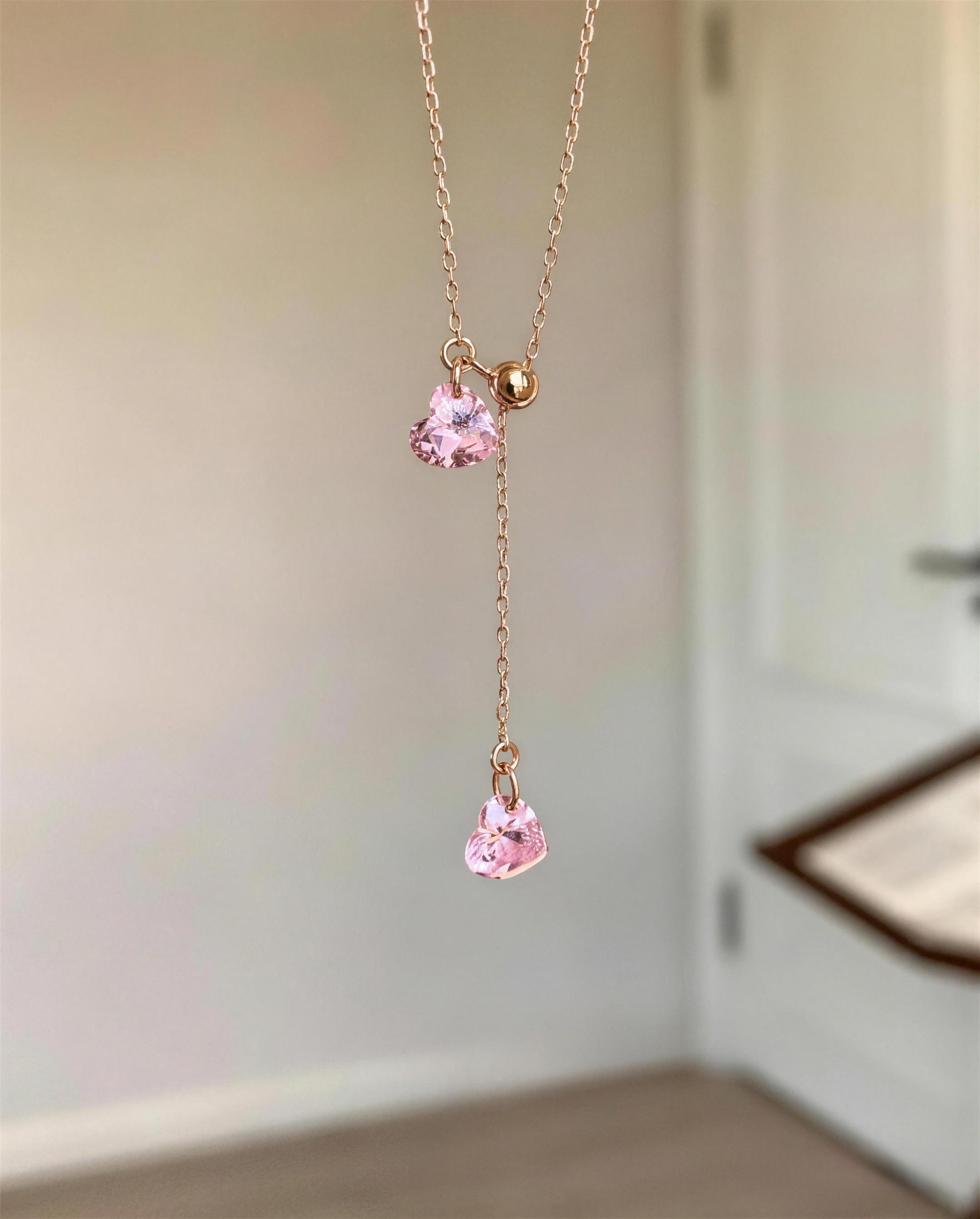 ose gold Y-necklace featuring two sparkling pink heart-shaped cubic zirconia stones with an adjustable gold slider bead suspended indoors
