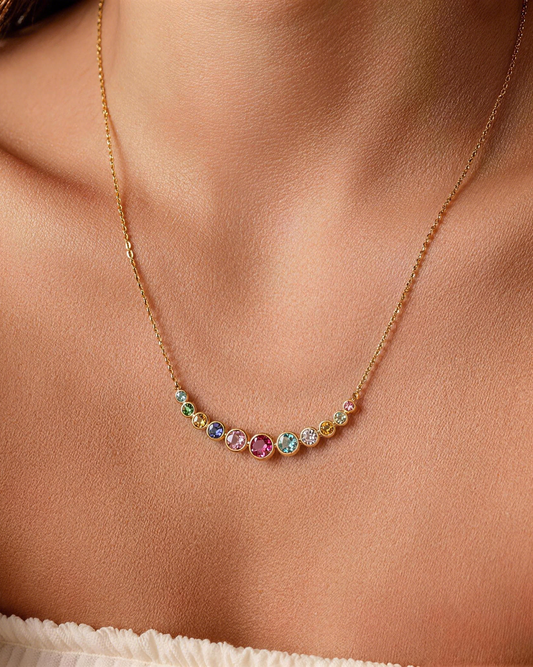 Gold necklace with a curved arc of round bezel-set multi-colored cubic zirconia stones worn on a person's collarbone