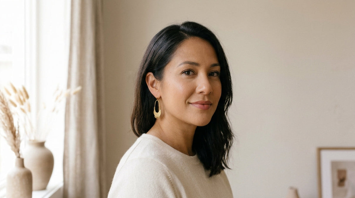 Woman wearing medium-length gold drop earrings in a softly lit three-quarter portrait.