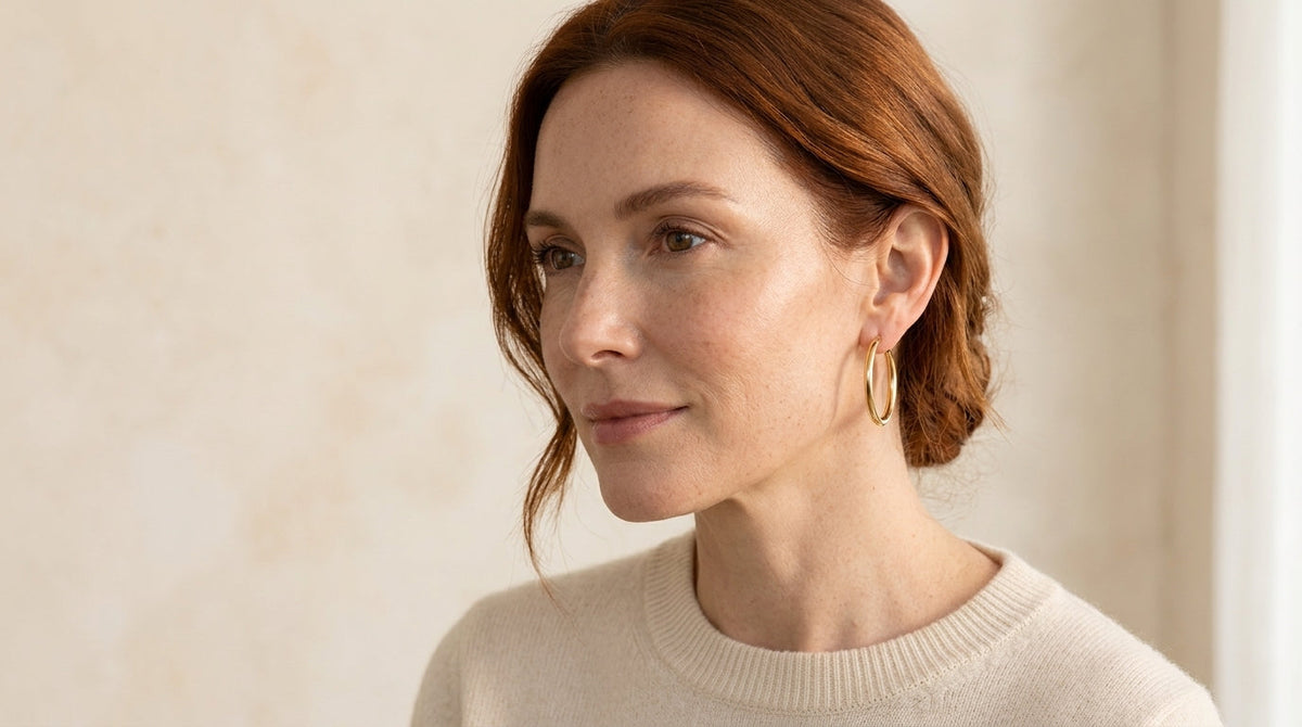 Woman wearing a medium-sized gold-tone hoop earring with her hair tucked behind one ear